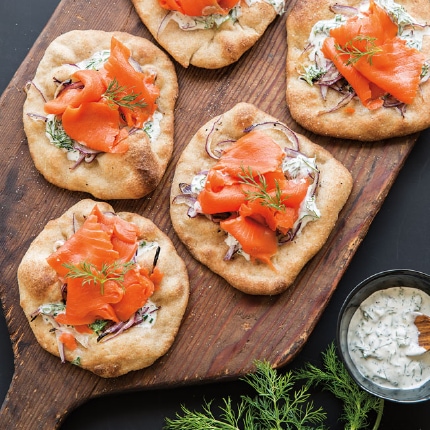 Smoked salmon and red onion pizzettes served on a wooden cutting board with fresh dill. 