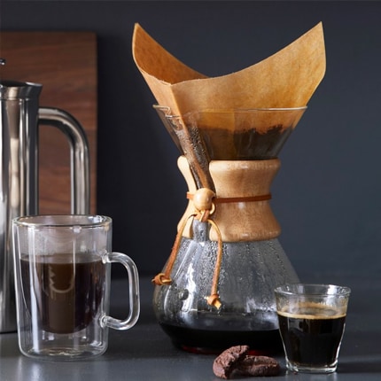 Chemex pour over carafe with double walled glass mug and small glass of coffee with chocolate cookie.