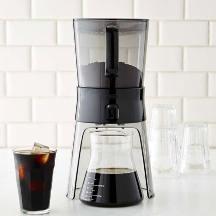 OXO cold brew coffee maker brewing into a glass carafe next to a glass of iced coffee.