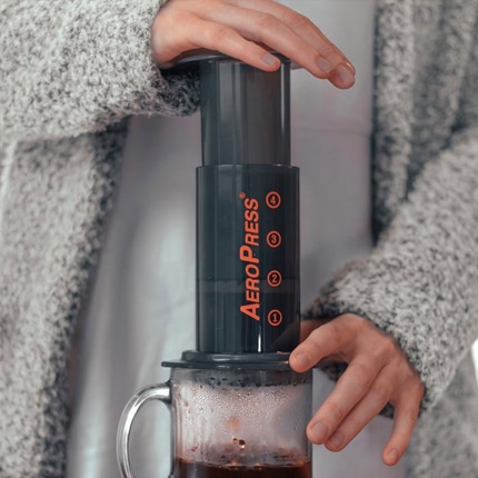 Person in a gray sweater pressing coffee from an AeroPress coffee maker into a cup.