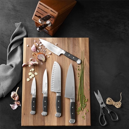 Boos edge-grain wooden cutting board with multiple knives, shallots, napkin, shears, twine, napkin and knife holder.