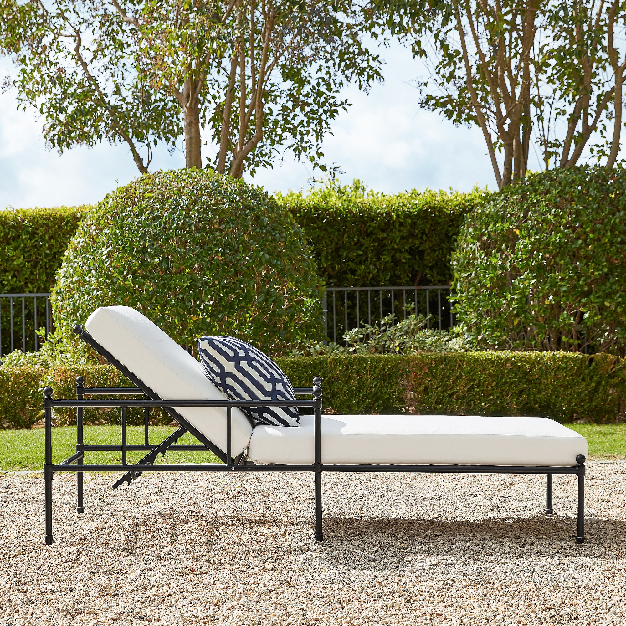 Close-up of the white cushioned armchair showing black metal frame and armrest supports in a garden setting.