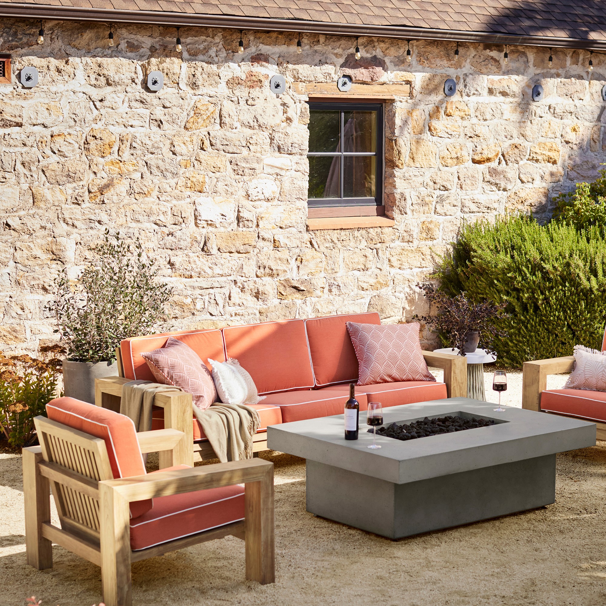 Outdoor seating set with coral cushions and concrete fire pit table, modular wooden frame, garden backdrop