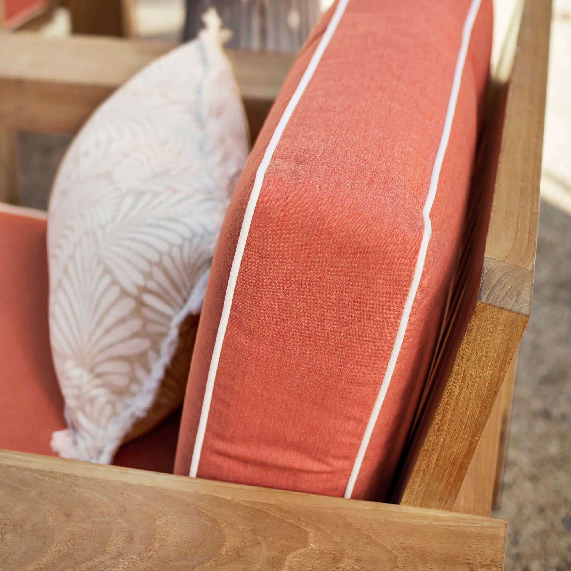 Close-up of coral outdoor chair cushion with white piping on wooden armchair frame