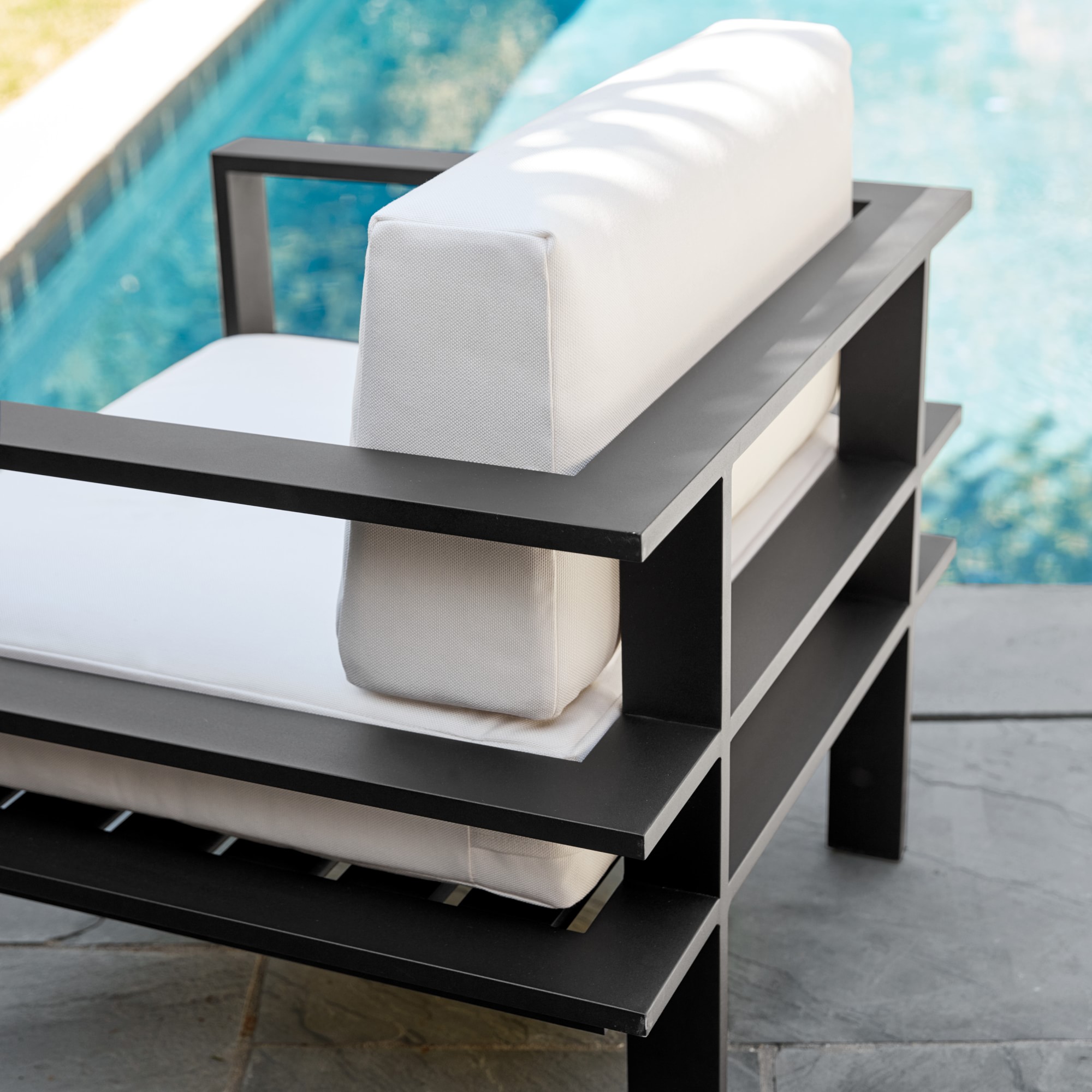 Patio with seating and stone wall in background; metal-framed furniture with white cushions.