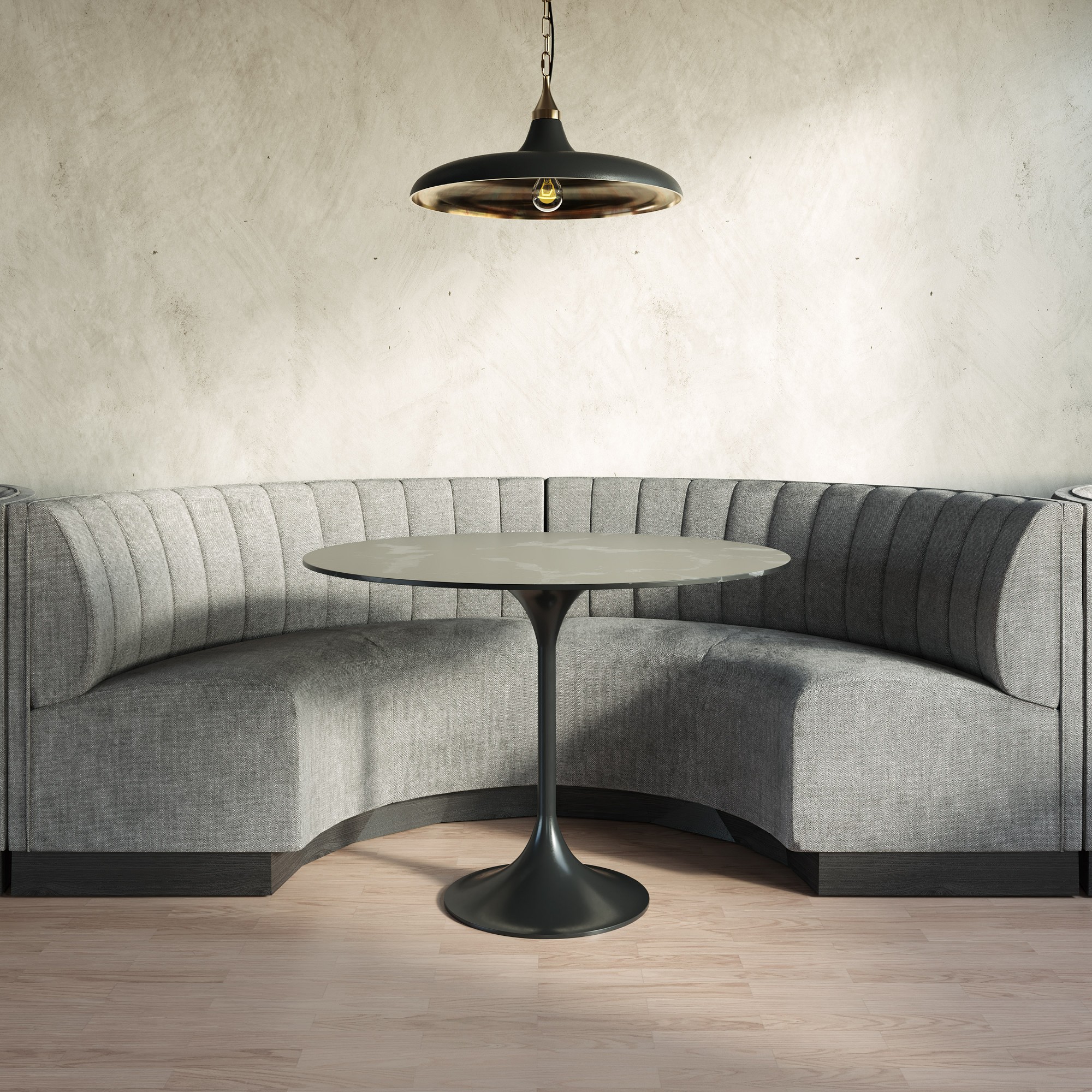 A modern round table with a curved gray sofa booth and a pendant light above.