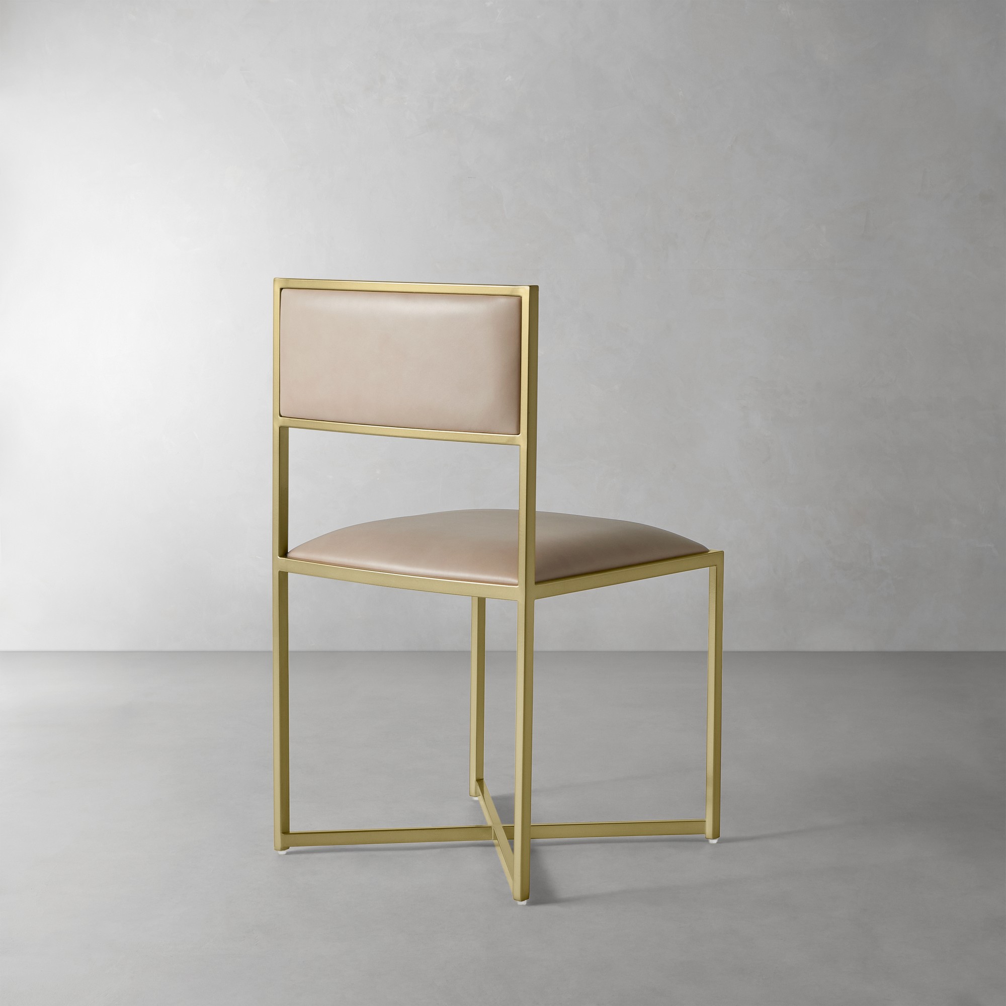 Rear three-quarter view of a gold-framed tan upholstered chair in a studio.
