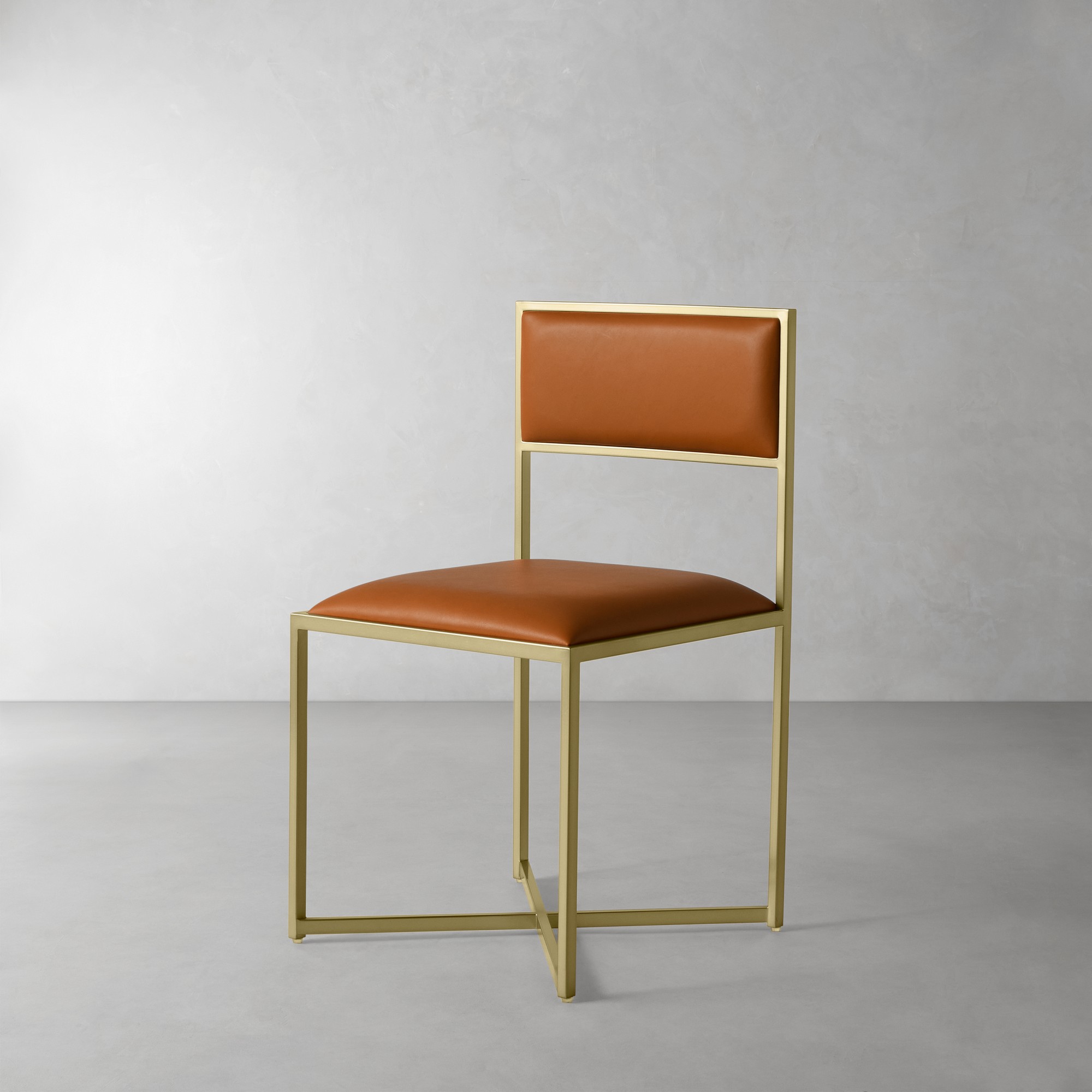 Chair with gold metal frame and light brown upholstery shown in a studio setting.