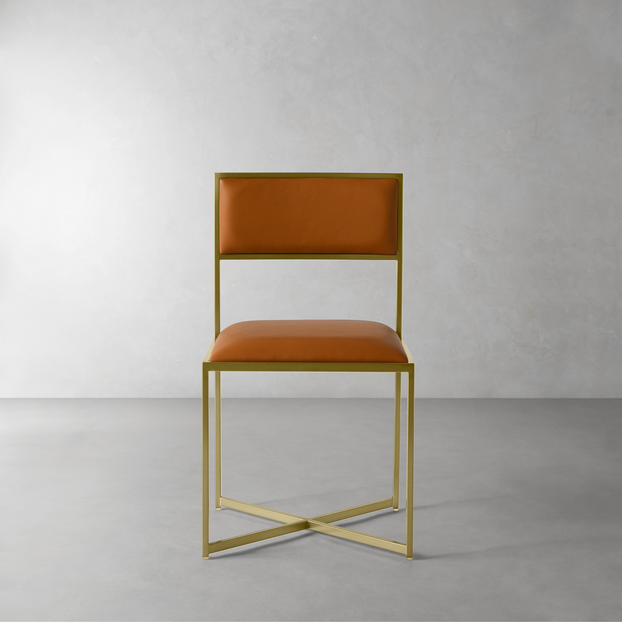 Chair with golden metal frame and orange-brown upholstered seat and backrest, set against a light gray background.