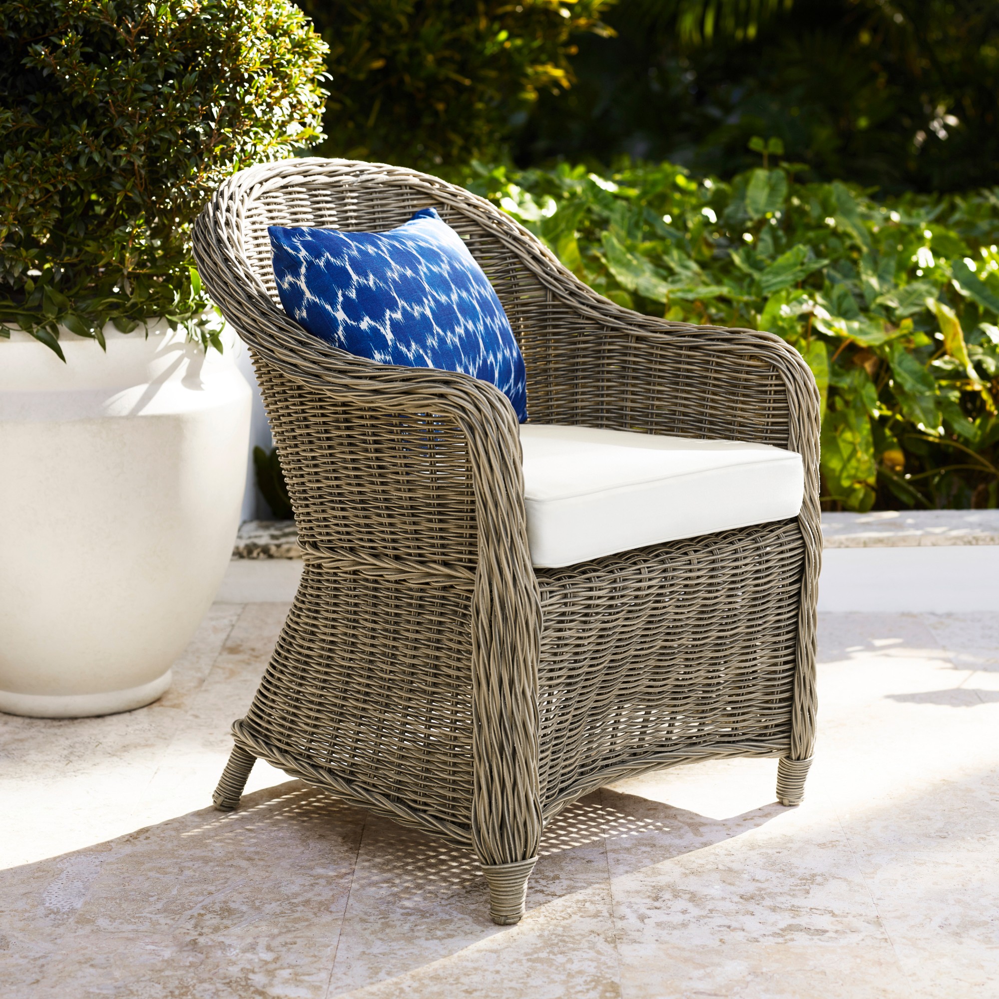 Wicker lounge chair with white cushion and blue patterned pillow in an outdoor setting
