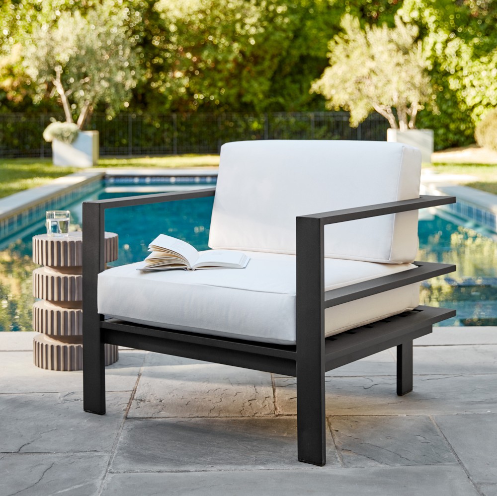 Modern outdoor lounge set with white cushions and black metal frame by pool, includes armchair, loveseat, coffee table.