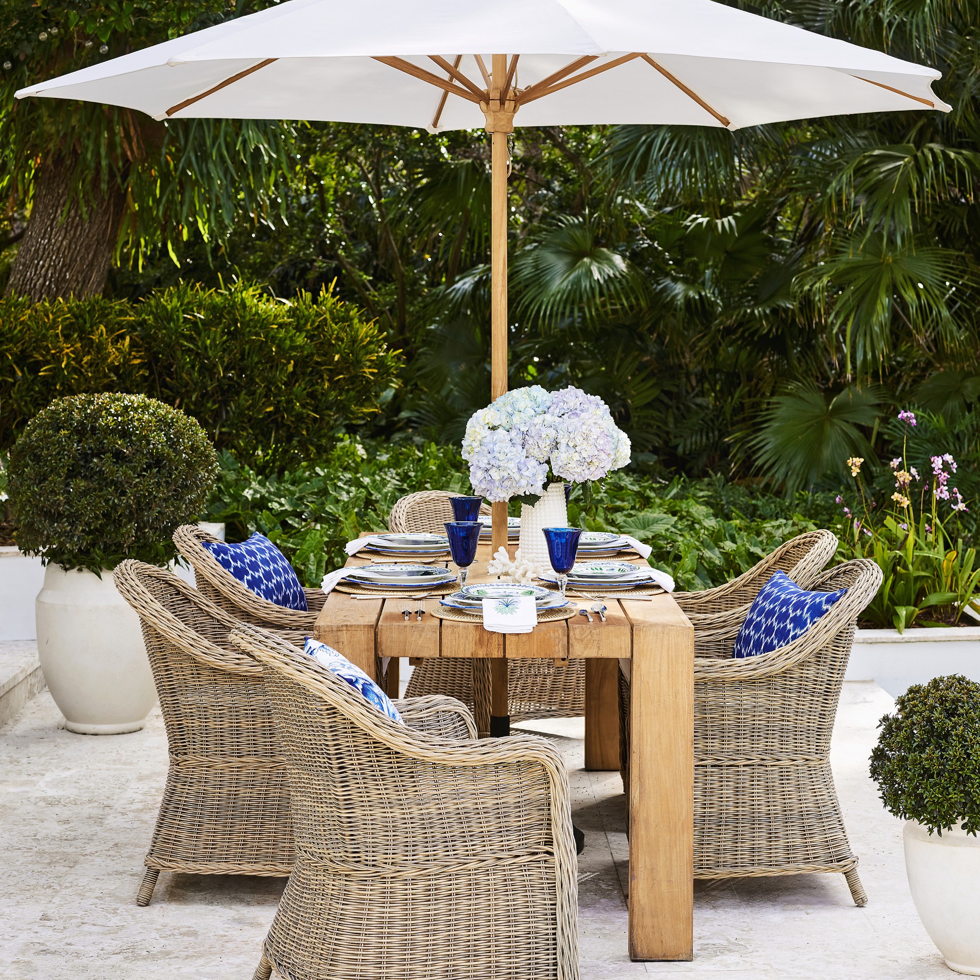Outdoor dining table with wicker chairs under a large white umbrella