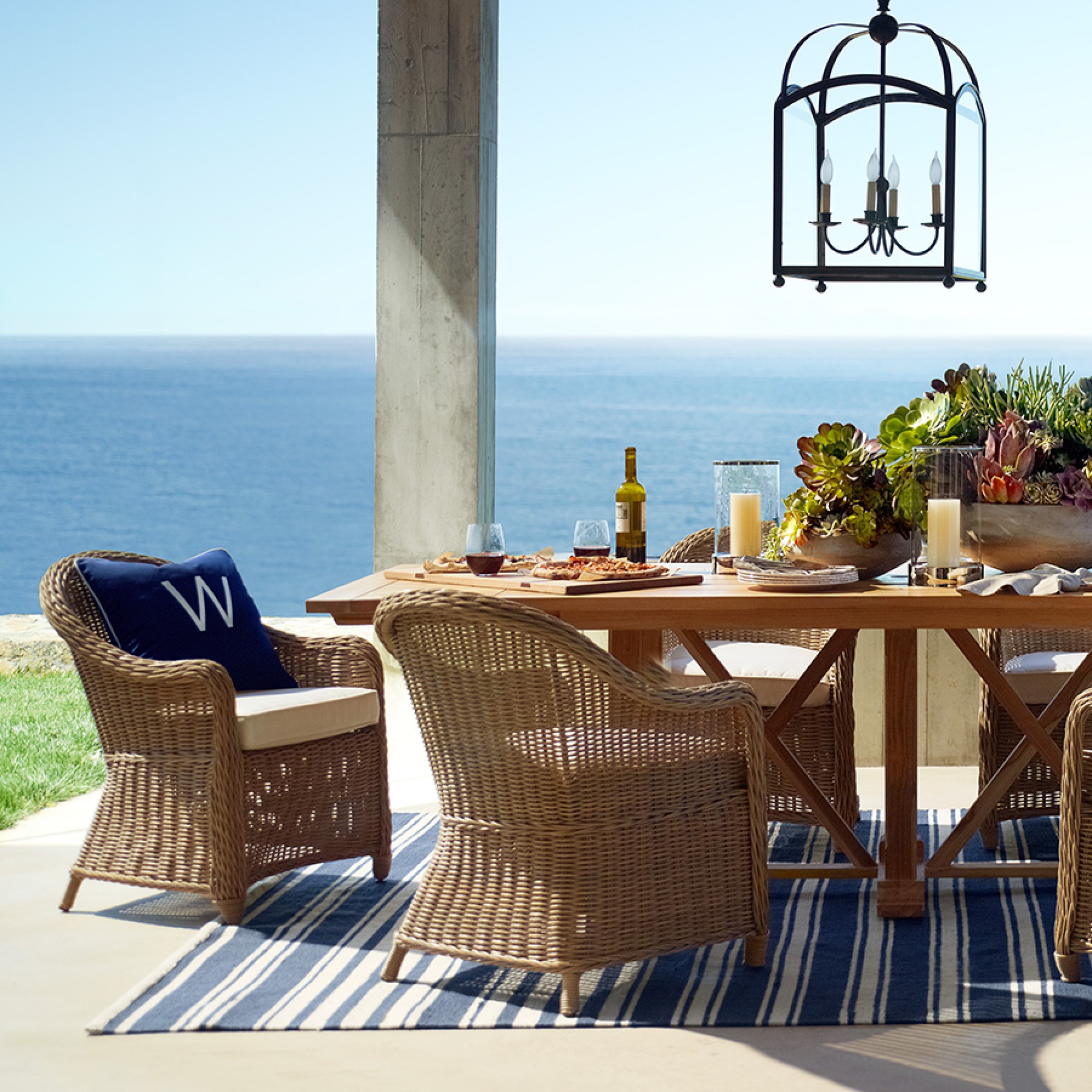 Outdoor dining table set by the sea with wicker chairs and blue glasses
