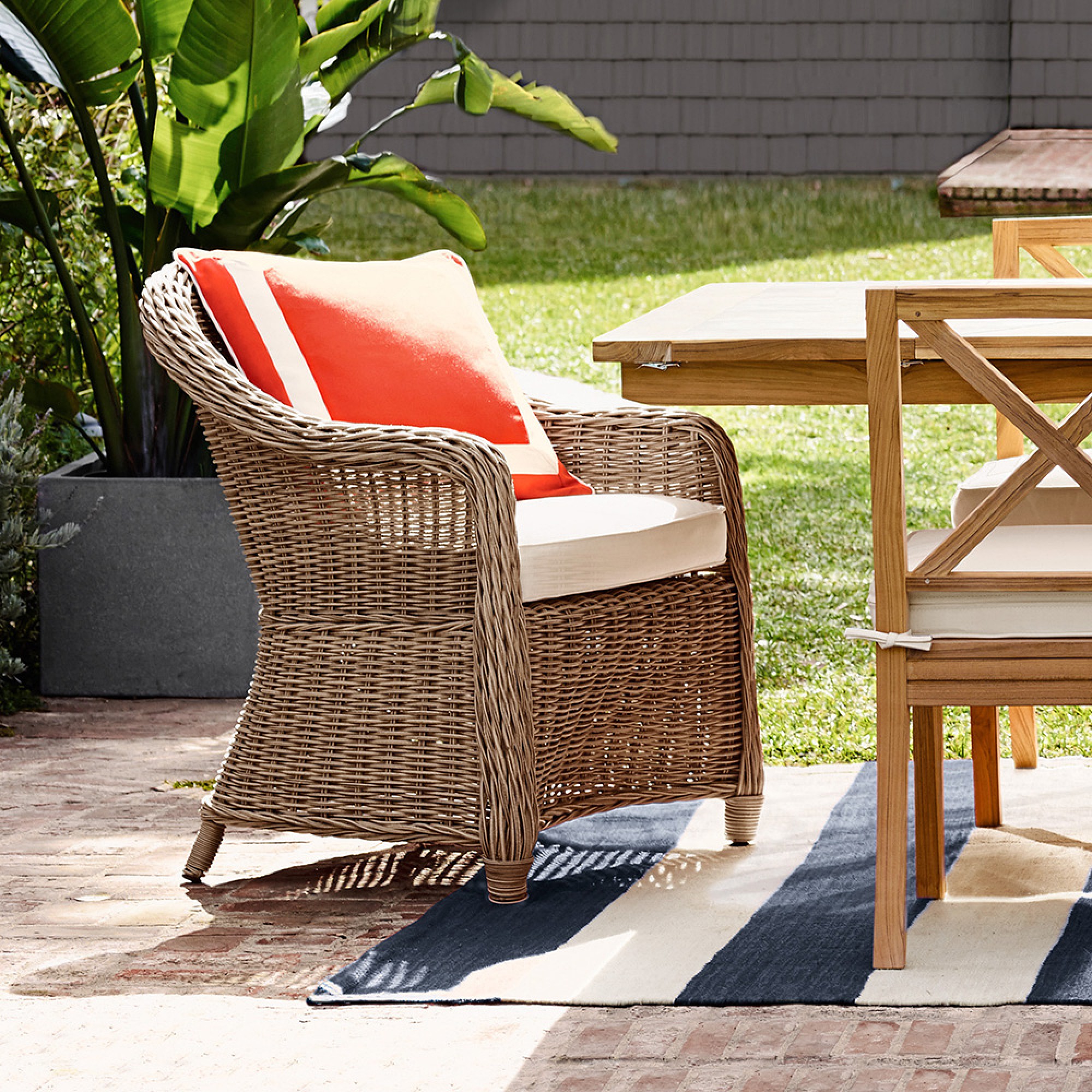 Outdoor dining set with wicker chairs and coral throw pillow on chair, beige cushions