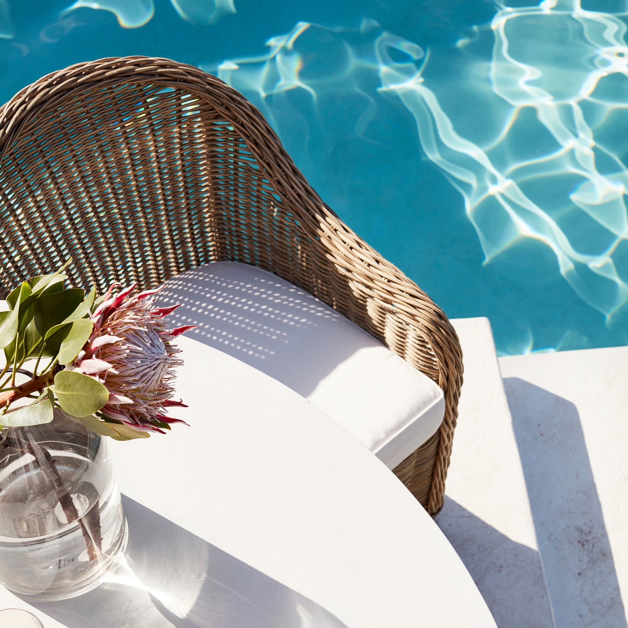 Wicker chair by a pool with glass vase of flowers