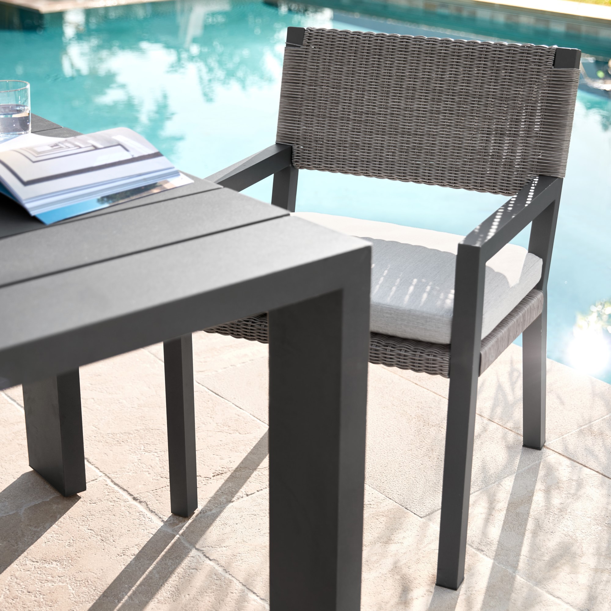 Patio table by a pool with a bottle, glass and plate on the edge.