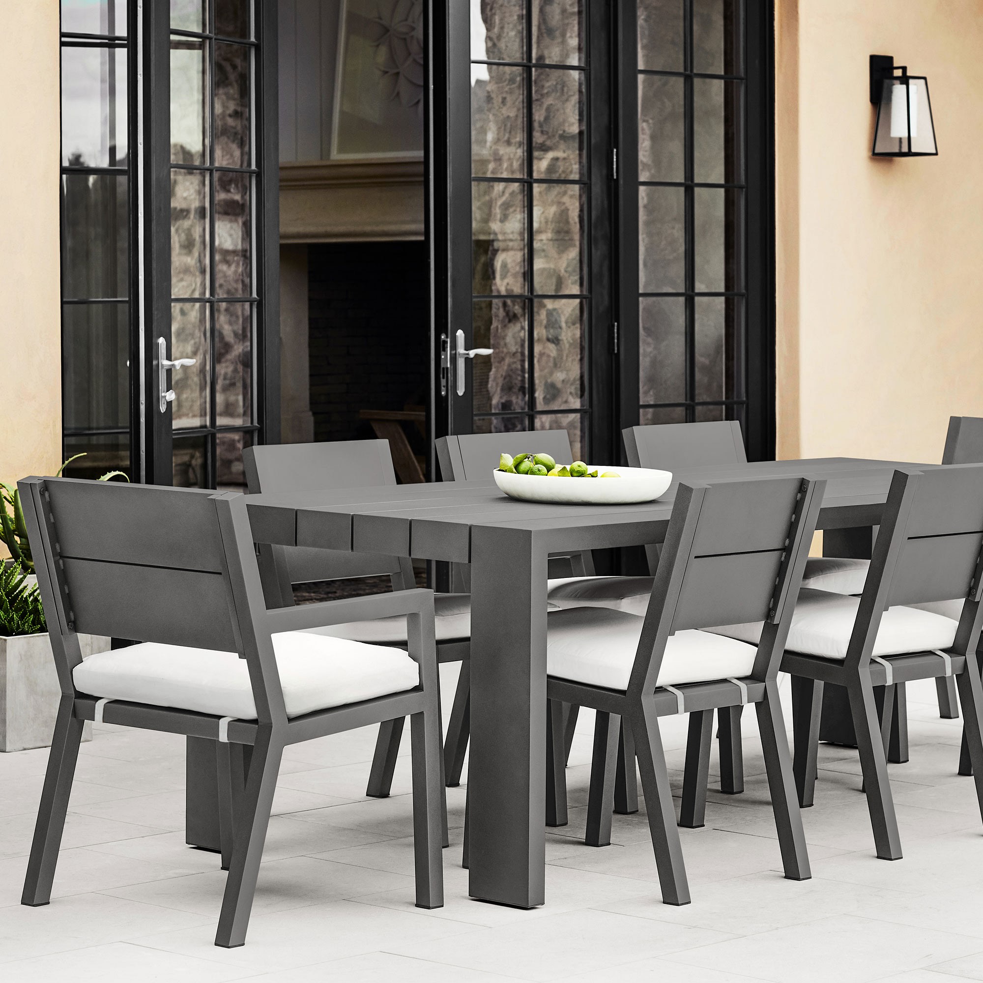 Outdoor dining set with multiple chairs around a table near a fireplace, modern gray metal furniture.