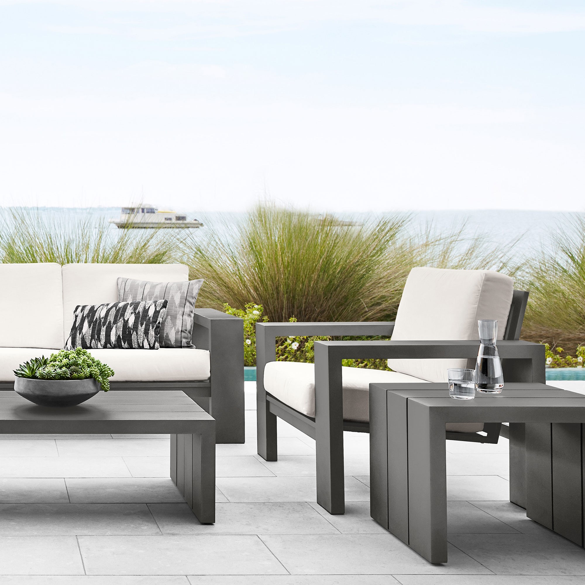 Close-up of a gray modular outdoor coffee table set with sofa in background and bowls of greens