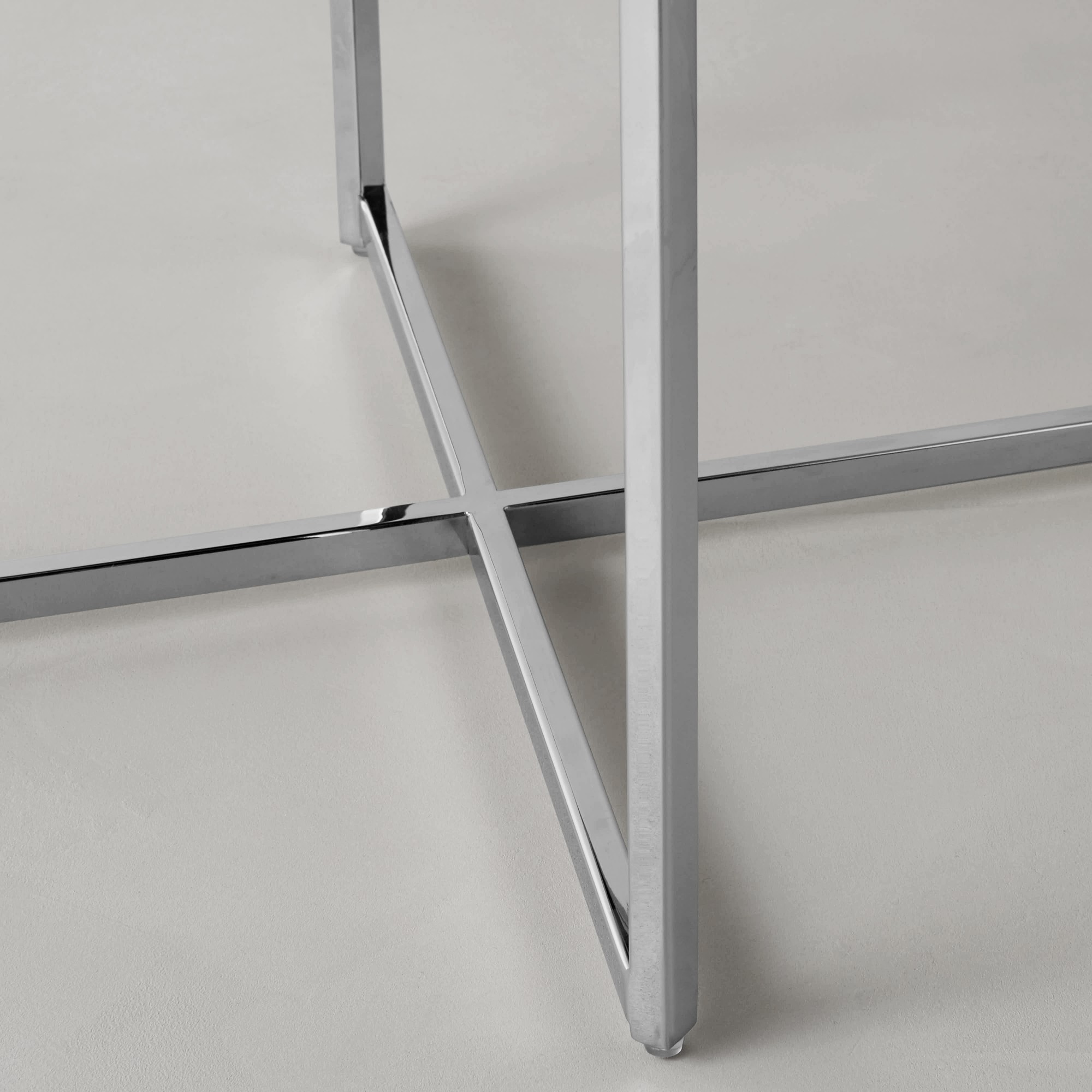 Close-up of the chair leg junction with cross brace in chrome finish on a light surface.