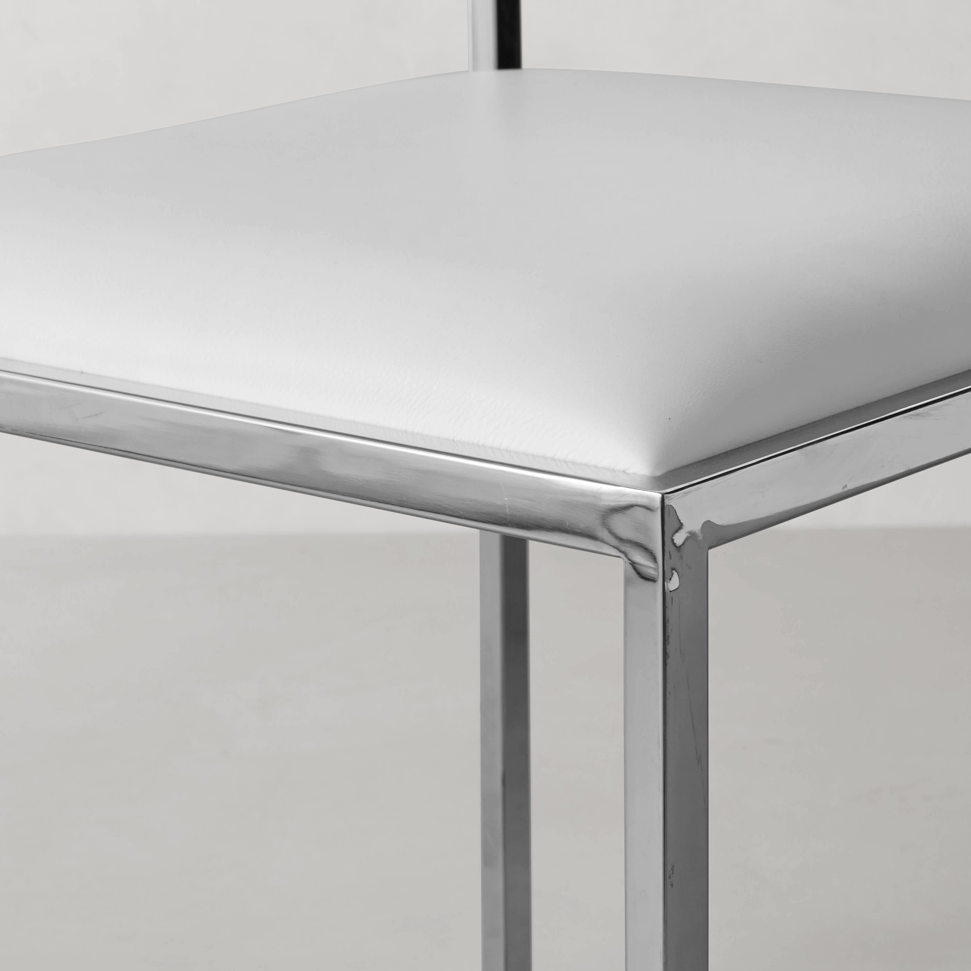Edge detail of a chrome chair frame meeting a white upholstered seat, showing joint and chrome finish.