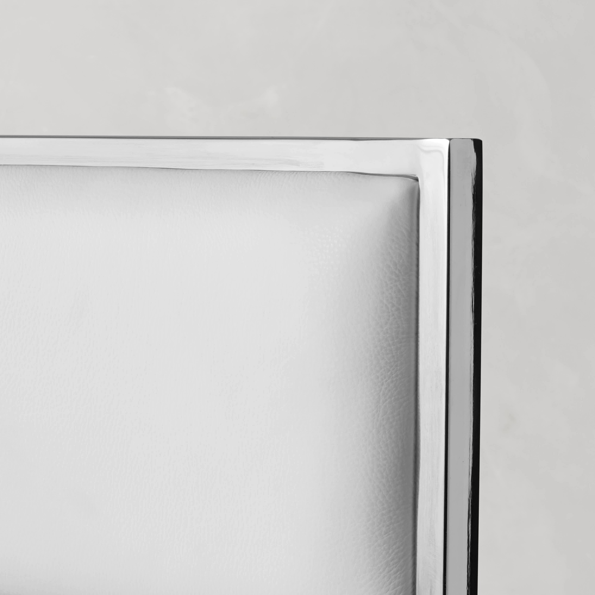 Close-up of the top edge of a white upholstered chair back showing stitching and chrome frame.