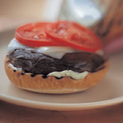 Grilled portobello mushroom burger topped with cheese and tomato slices.