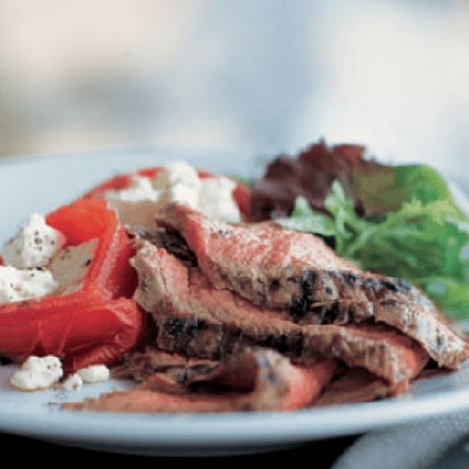Herbed flank steak with tomatoes lettuce and feta cheese on a plate.