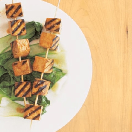 Grilled tofu kabobs with spicy marinade presented on a bed of greens.