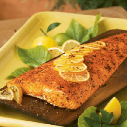 Cedar planked salmon with seasoned lemon butter in a serving dish topped with lemon slices.
