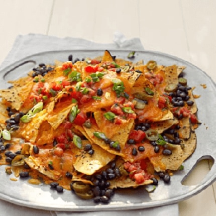 A serving dish holding a pile of grilled nachos with black beans salsa and jalapenos.