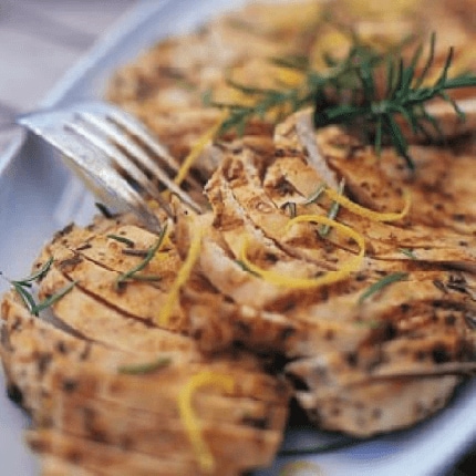 Lemon herb chicken breasts sliced with lemon shavings and thyme on a plate.