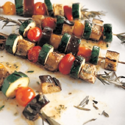 Marinated summer vegetables grilled on rosemary skewers displayed on a plate.