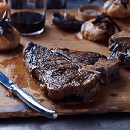 Grilled porterhouse steak with Romesco on chopping board.