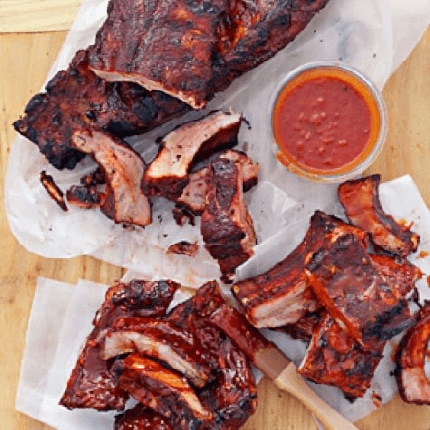Memphis style baby back ribs on grease proof paper with a spicy dip.