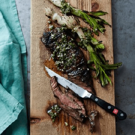Grilled skirt steak with chimichurri on a wooden board.