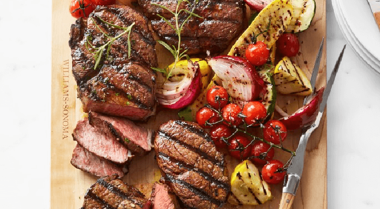 Steak and grilled vegetables on a wooden board.