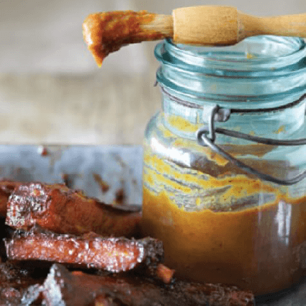 Jar of peach barbecue sauce next to two pieces of glazed steak.