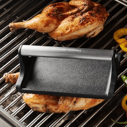 Chicken on grill being pressed down by a grill press.