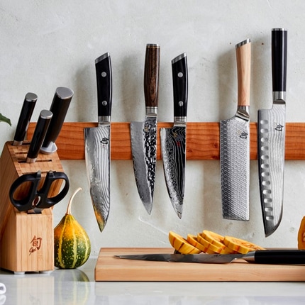 Several Japanese-style kitchen knives on a magnetic bar above a kitchen counter with sliced squash.