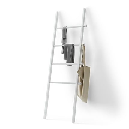 An Umbra Blanket Ladder leaning against a white wall with a bag and two towels hanging from it.