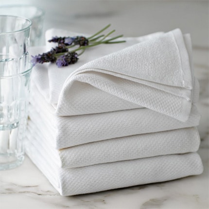 Stack of white All Purpose Pantry Towels on a counter next to glass of water.