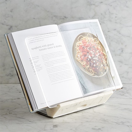 A Marble Cookbook Holder propping a cookbook open to a spaghetti recipe.