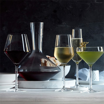 Set of Schott Zwiesel stemware with different types of wine arranged on a counter with a carafe of red wine and a bowl of crackers.