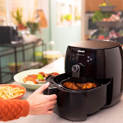omeone pulling out a tray of roasted chicken from Philips Premium Digital Air Fryer next to a bowl of french fries.