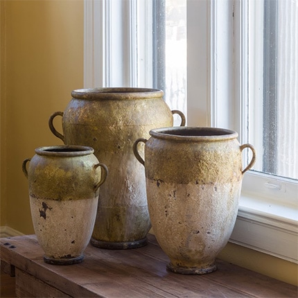 Set of three metal French-style garden pots arranged in front of a window on a wooden counter.