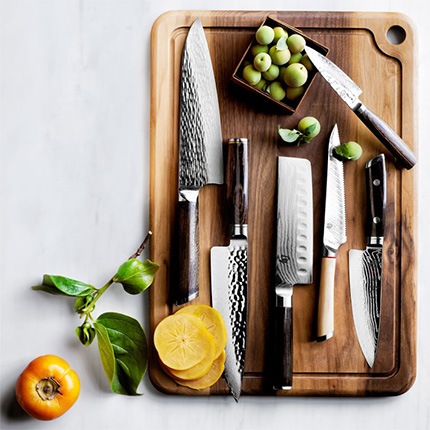 Set of Shun knives including Classic Hollow-Ground Nakiri Knife on a wooden cutting board with sliced fruit.