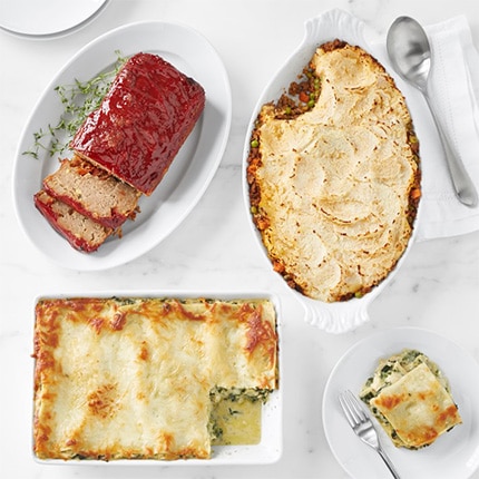 Meat loaf, shepherd’s pie, and other meal delivery entrees in white ceramic serving dishes arranged on a countertop.