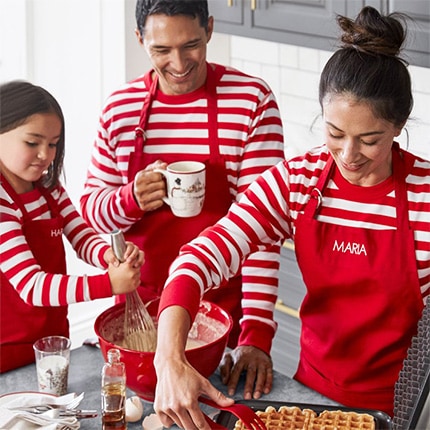Two parents and a child cooking waffles together and wearing red personalized aprons.