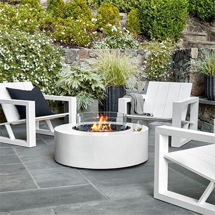 White chairs surrounding an EcoSmart Fire Table Ark 40 with a glass of white wine on the edge in a backyard.
