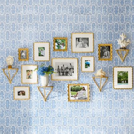 A set of photos displayed in gold AERIN Wave gallery frames arranged on a wall with blue printed wallpaper.
